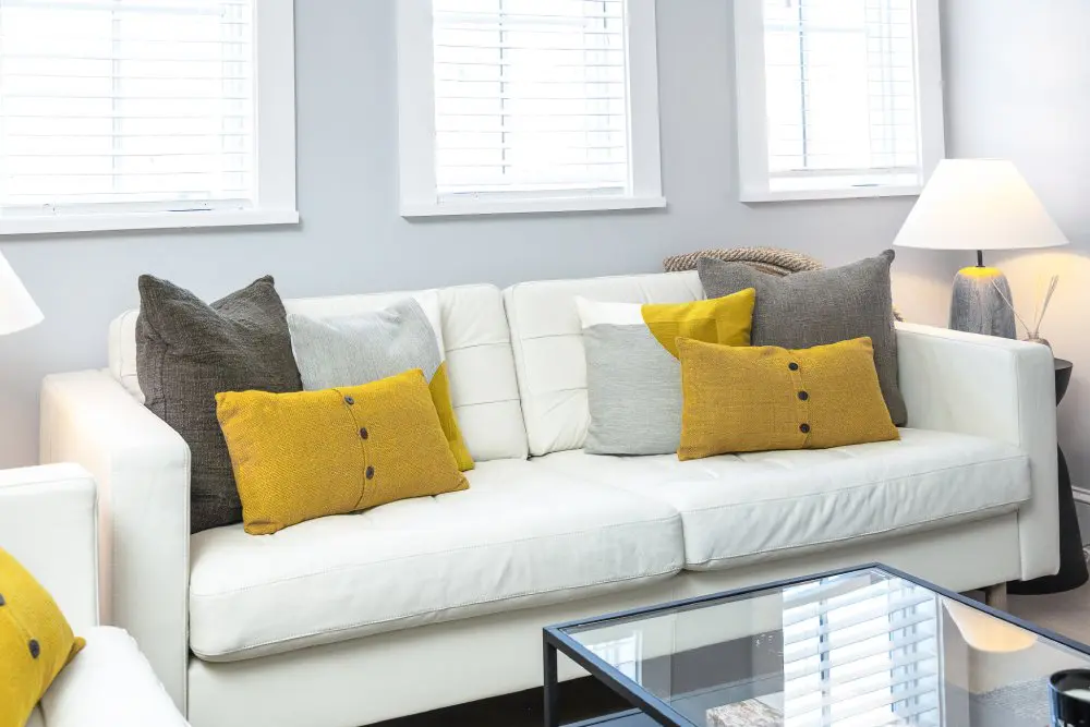 Close up of white couch with colorful yellow and gray pillows.