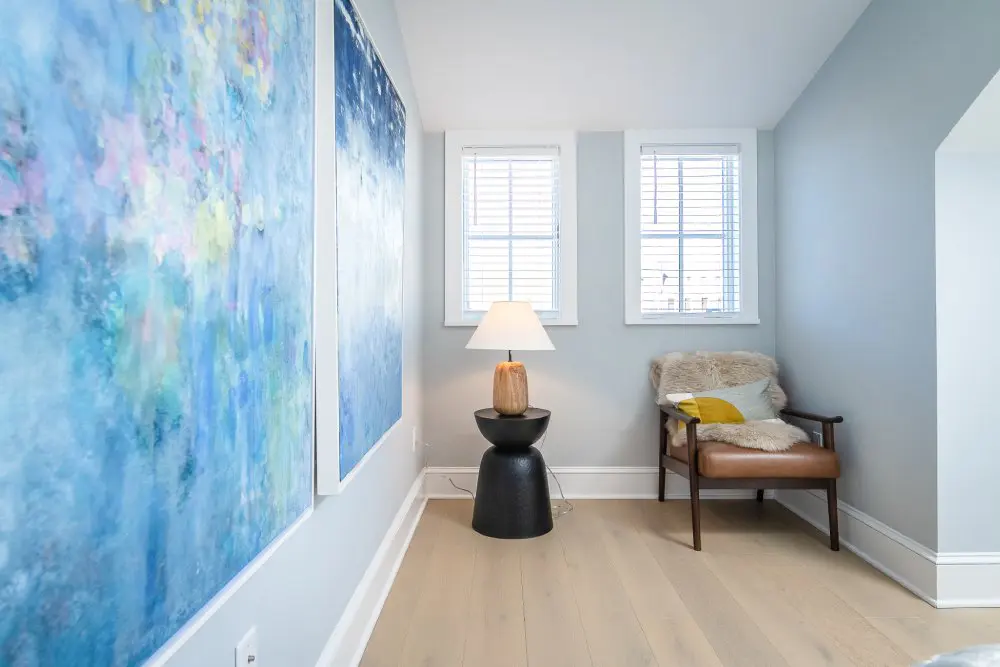 Abstract blue, pink, and yellow art hangs on wall leading to two bedroom windows.