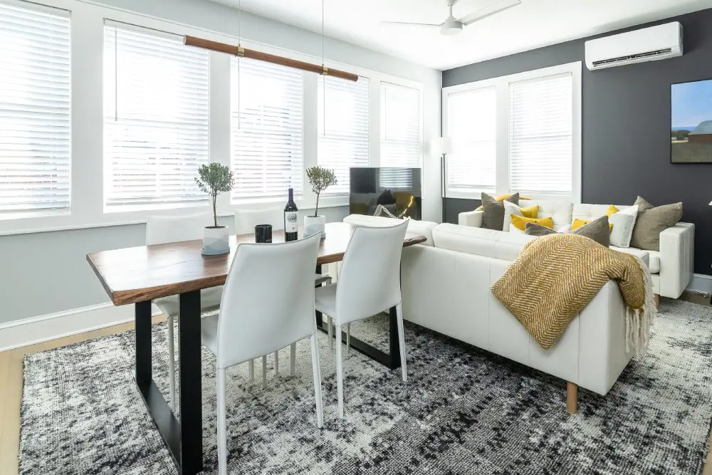 Large wooden table sits beside bright windows in apartment living room.