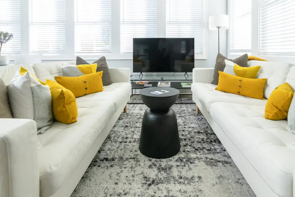 Looking between two big white couches toward a tv and bright windows behind it.